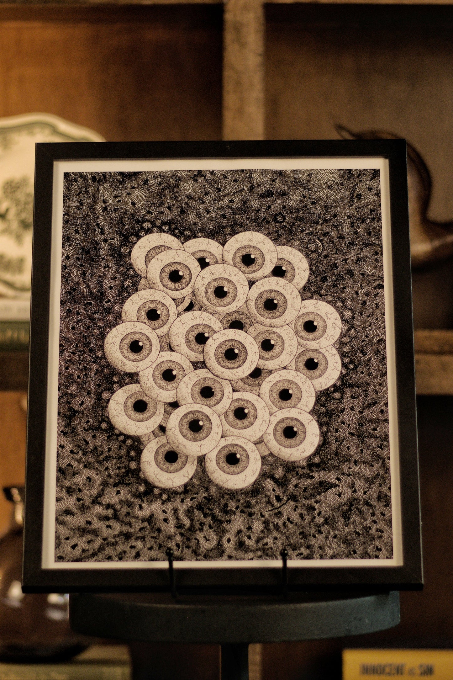 Framed black and white pattern on a stand with a bookshelf in the background