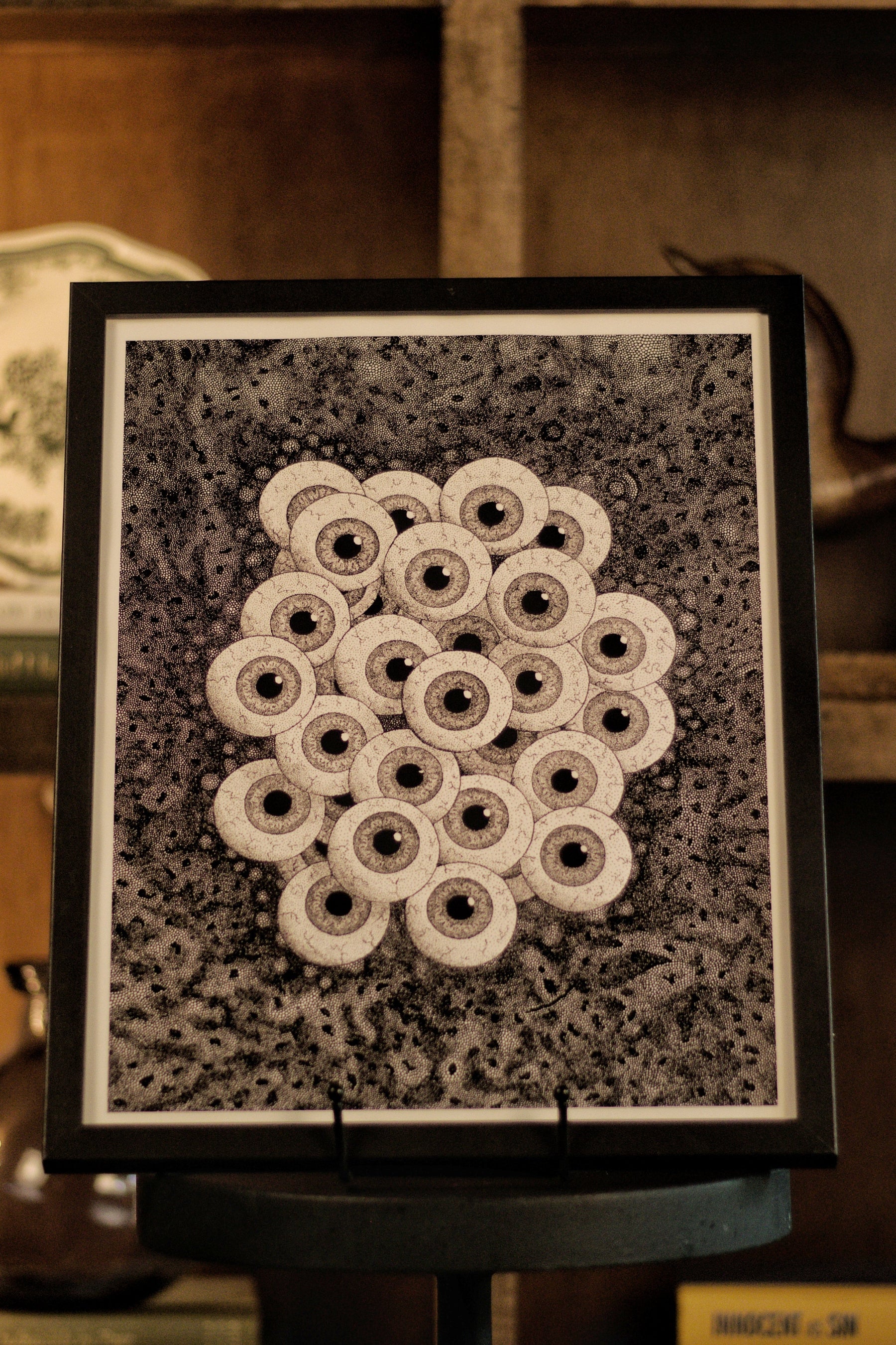 Framed black and white pattern on a stand with a bookshelf in the background